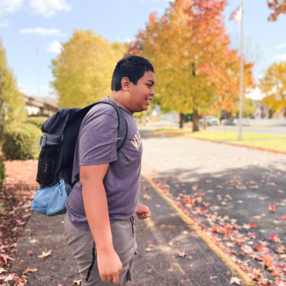 An Autistic Teenager Outside of His High School Smiling at the leaves.